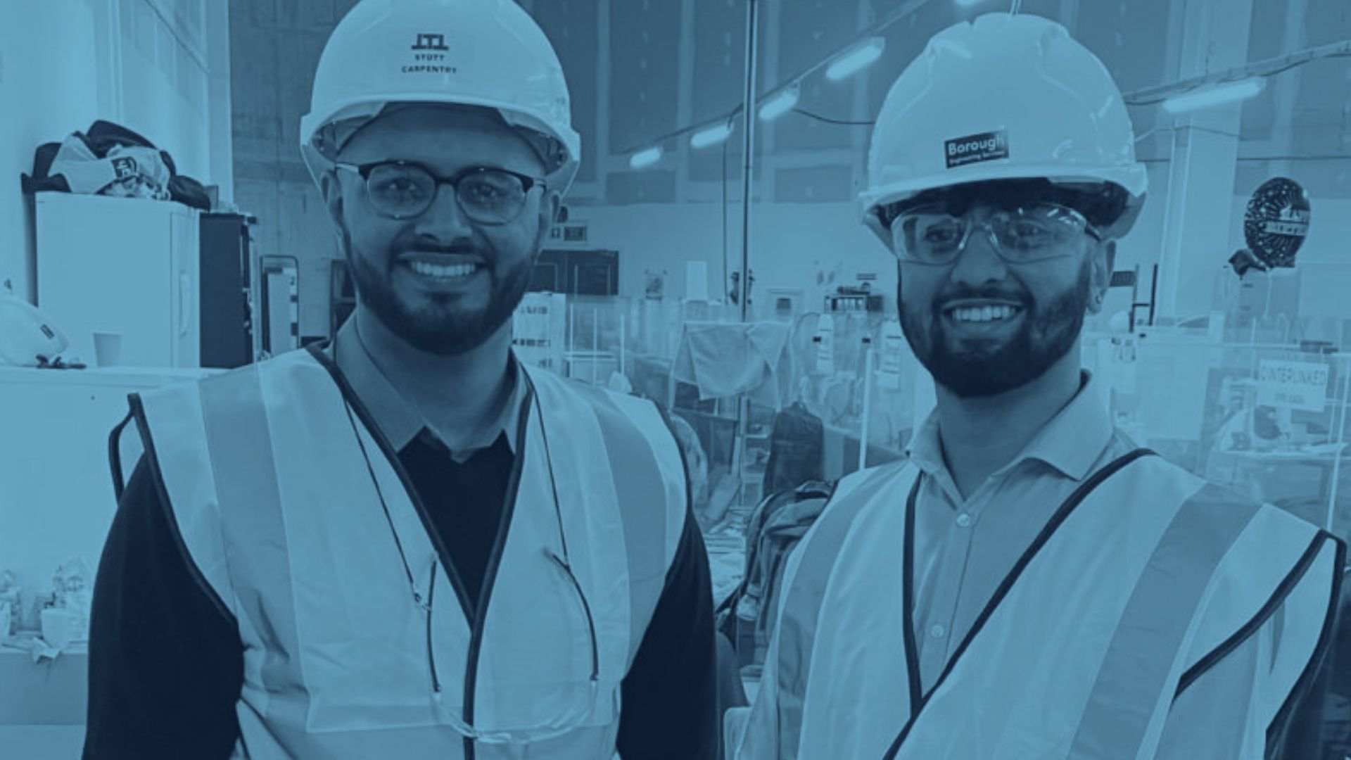 Two construction apprentices in hard hats and high-visibility vests smiling on a building site